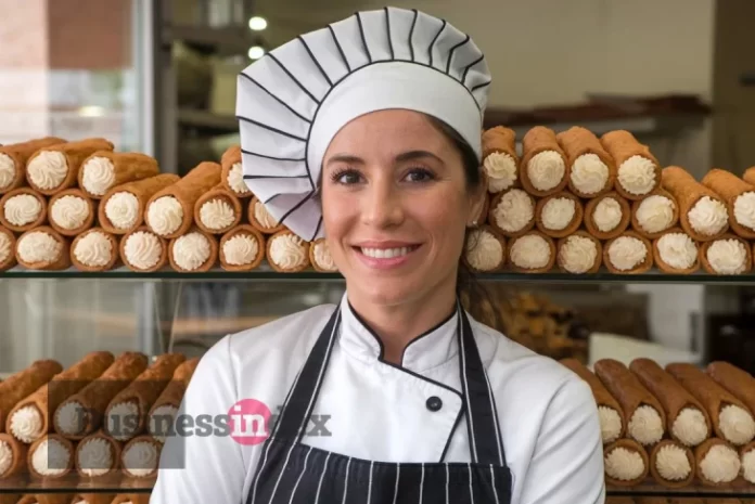 Cannoli Queen Amanda Labollita smiling while piping cream into a crispy cannoli shell.